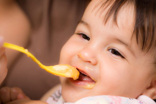 A cute baby is having spoonful of food