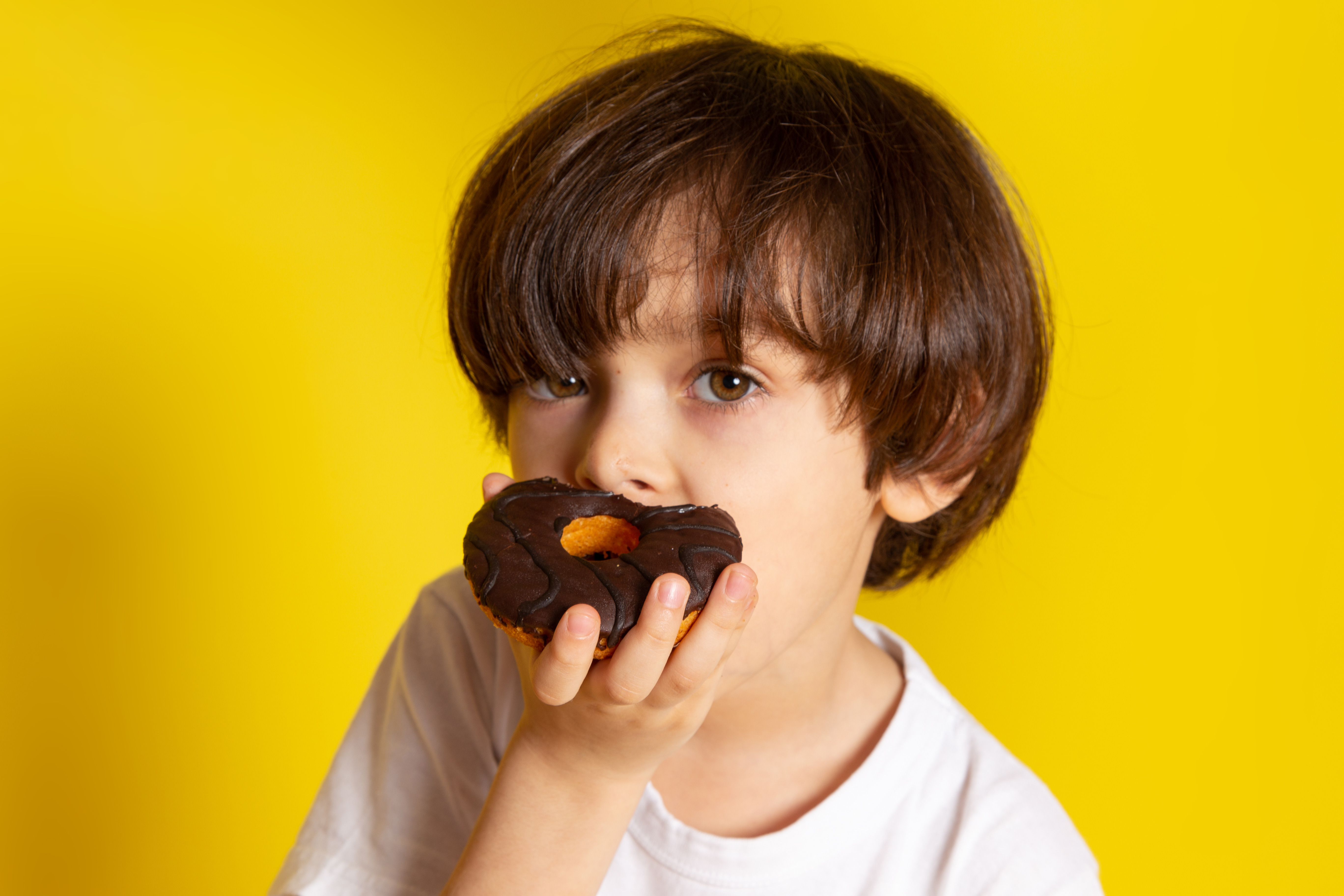front-view-boy-eating-choco-donuts-white-t-shirt-yellow-floor (1)
