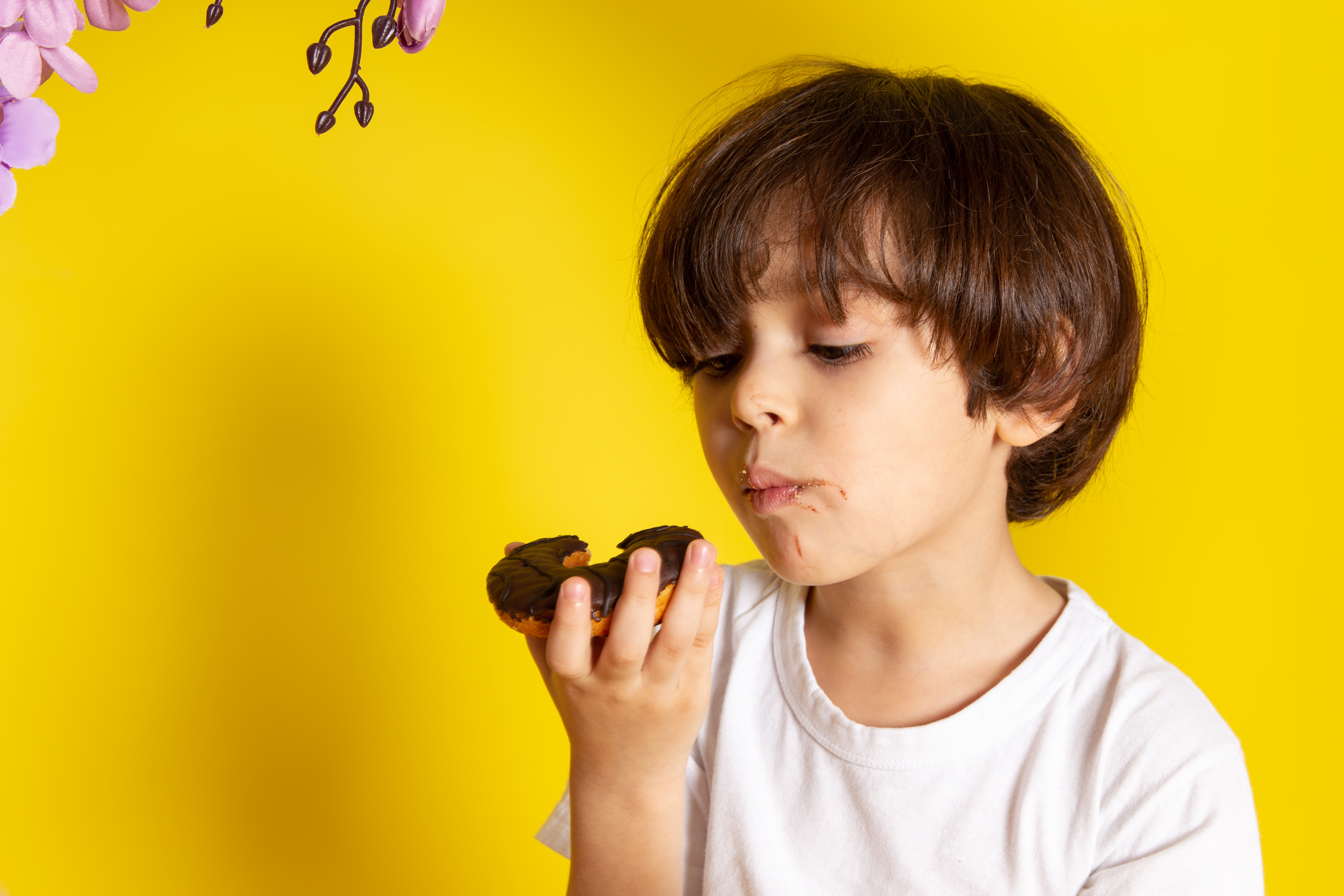 front-view-child-boy-white-t-shirt-eating-donuts-yellow-floor