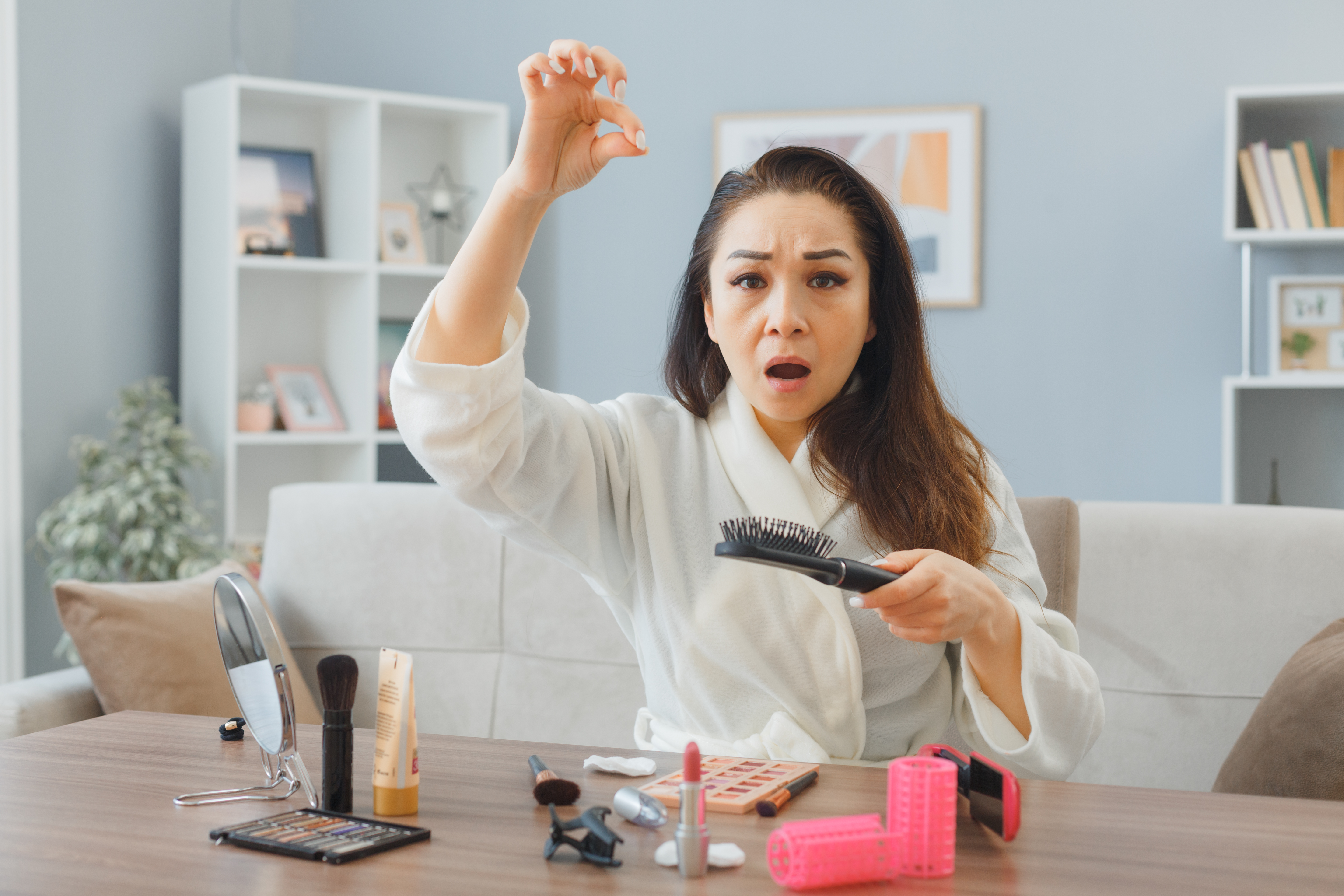 young-asian-woman-with-towel-bathrobe-sitting-dressing-table-home-interior-brushing-her-hair-being-confused-upset-having-hair-loss-doing-morning-makeup-routine